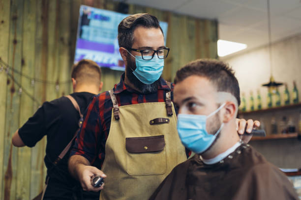 Hair cutting during pandemic. Young man have hair cutting at barber shop during pandemic isolation, they both wear protective equipment.