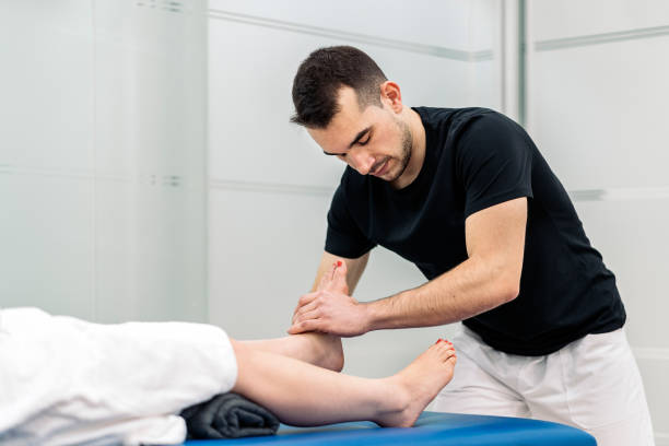 Male physiotherapist giving feet massage to unrecognized woman lying in stretcher.
