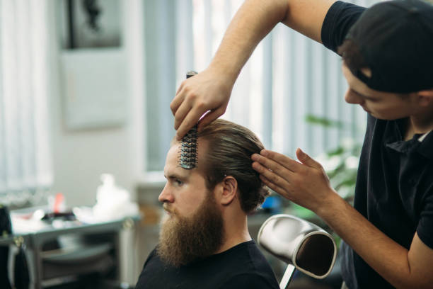 Master cuts hair and beard of men in the barbershop, hairdresser makes hairstyle for a young man.